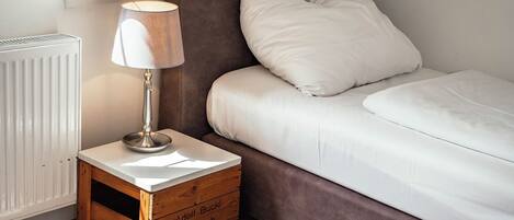 Une chambre avec un lit simple, une table de chevet avec une lampe, un radiateur et une caisse en bois.