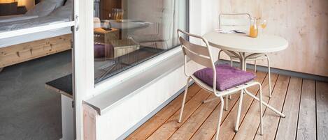 A room with a bed, a table with two glasses of orange juice, and a chair with a purple cushion.