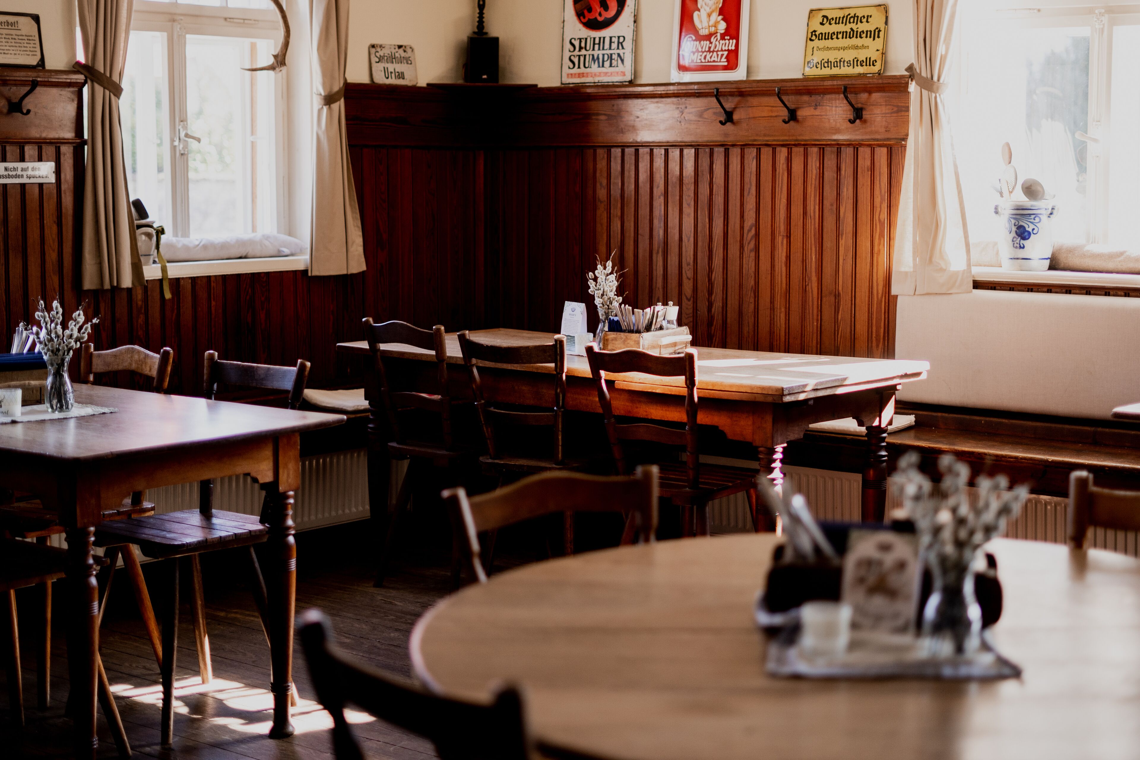 Interior de un restaurante con muebles de madera, una ventana con cortinas y un cartel sobre la ventana.