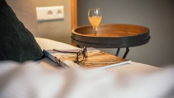 A bed with a book and glasses, a glass of wine on a small round table, and a pillow.