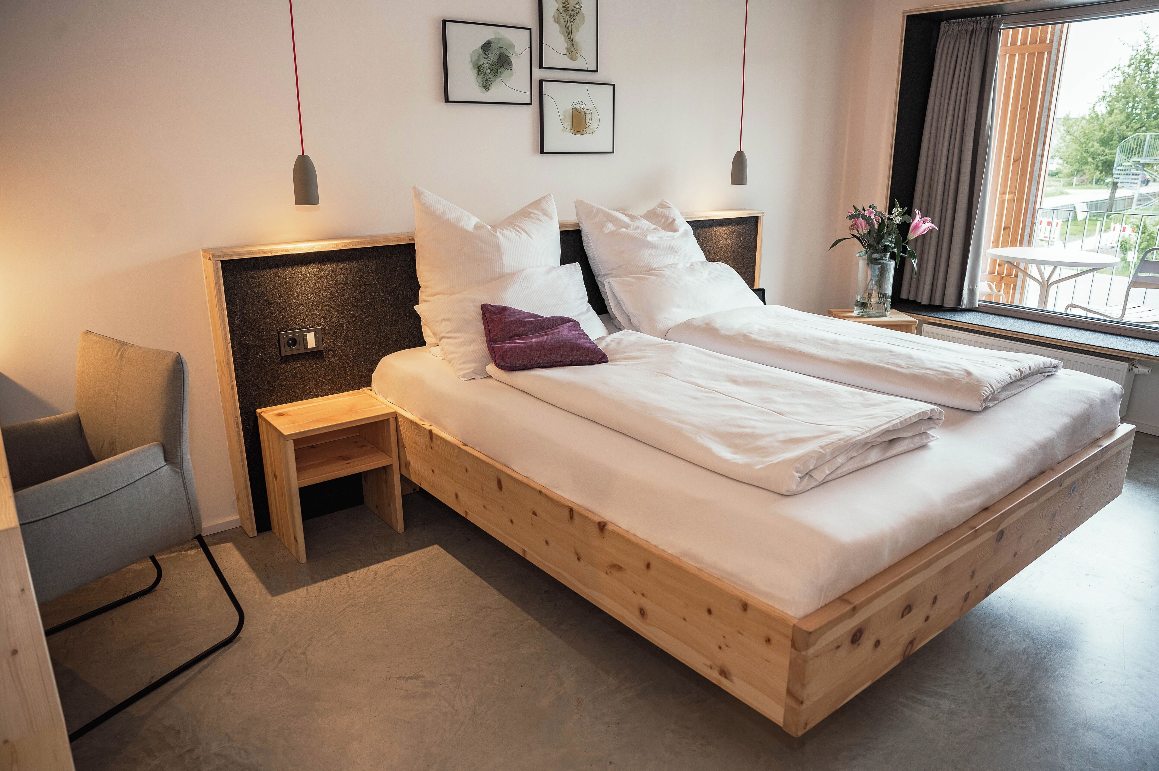 A modern bedroom with a wooden bed, a nightstand, a chair, and a window with a view of the outdoors.
