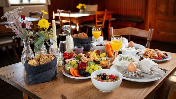A breakfast table with various food items, including fruits, bread, and a candle.