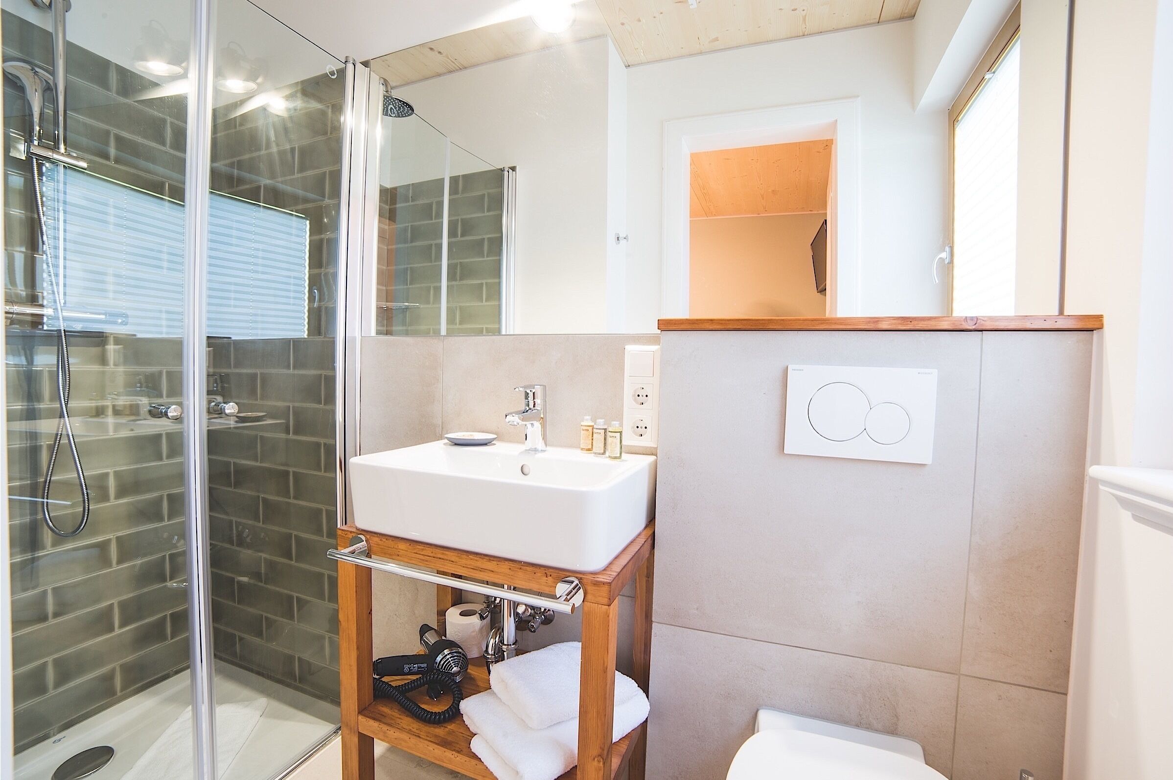 A modern bathroom with a glass-enclosed shower, a wooden vanity with a white sink, and a mirror above the sink.