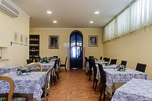 A dining area with tables set for six, each with a floral centerpiece. There are framed artworks on the walls and a large arched doorway. - Hotel Arcangelo (Viareggio)