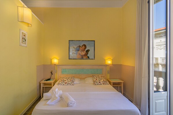 Habitación de hotel con una cama, dos mesitas de noche, un cuadro en la pared y una ventana con cortinas.