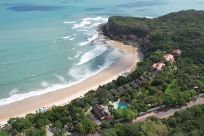 Vue aérienne d’un complexe hôtelier de bord de mer, avec une piscine, des parasols et différents types d’hébergements.