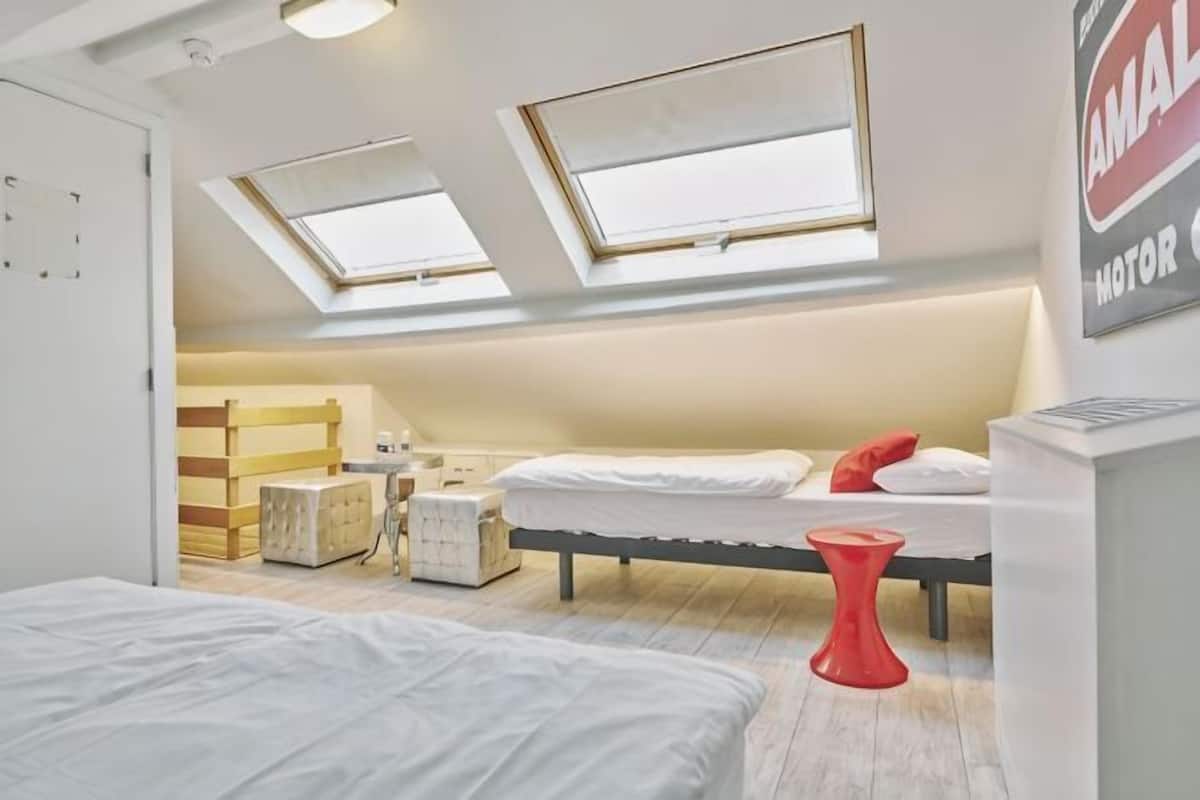 Een slaapkamer met twee bedden, dakramen, een rode kruk en een witte kast.