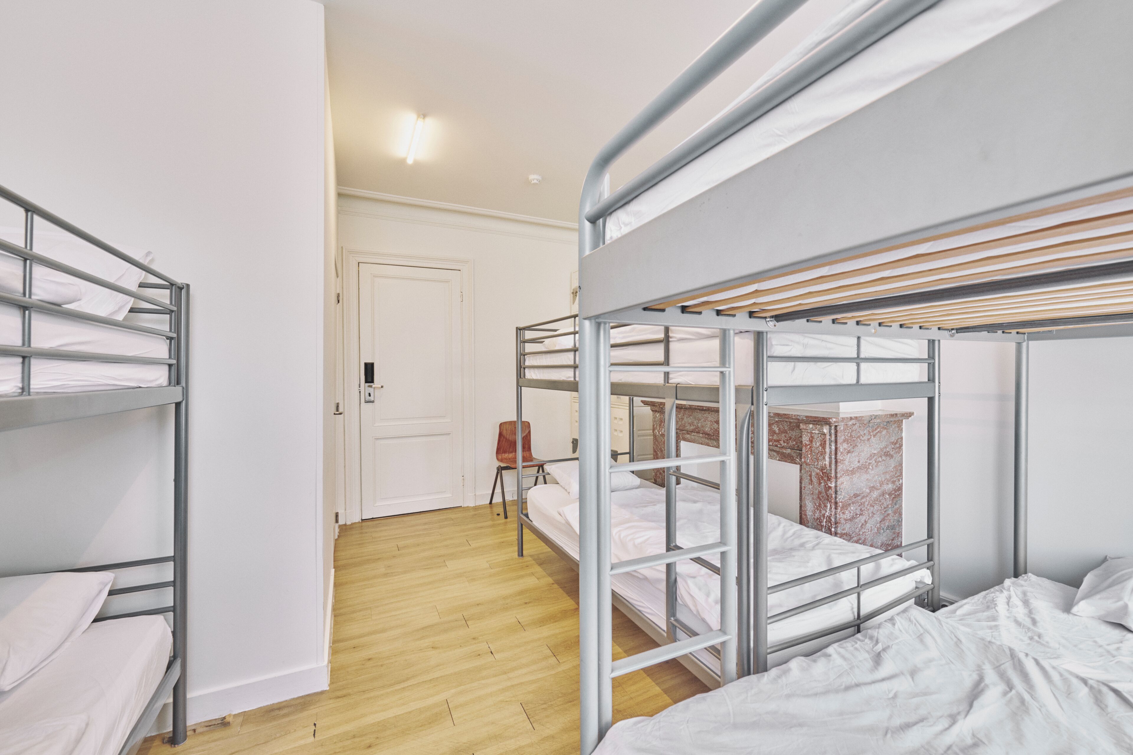 Een slaapzaal met stapelbedden, een houten vloer, een deur en een stoel.