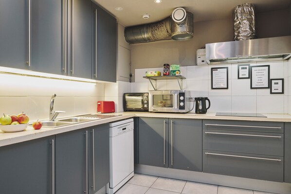 A modern kitchen with grey cabinets, a dishwasher, a microwave, a toaster, and a kettle.