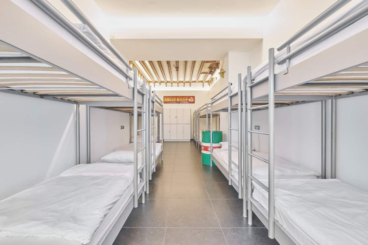 Een slaapkamer met stapelbedden van metaal, een betegelde vloer, en een bordje met de tekst 'Anglo-Belgese'.