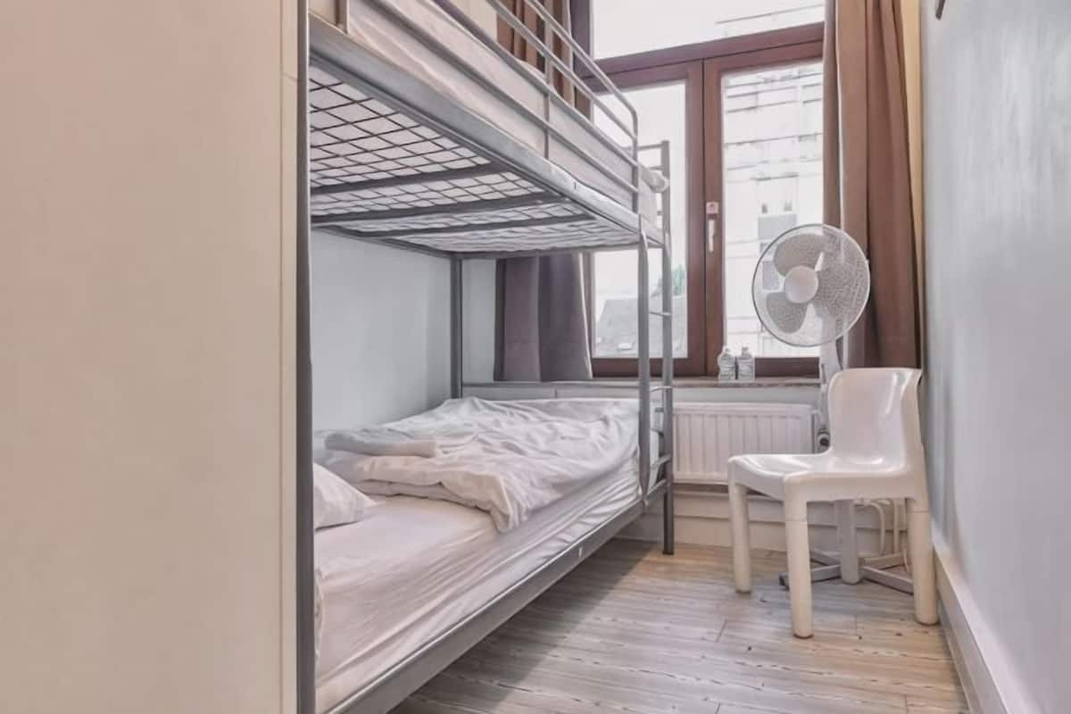 Een slaapkamer met een stapelbed, een radiator, een witte stoel en een raam met gordijnen.
