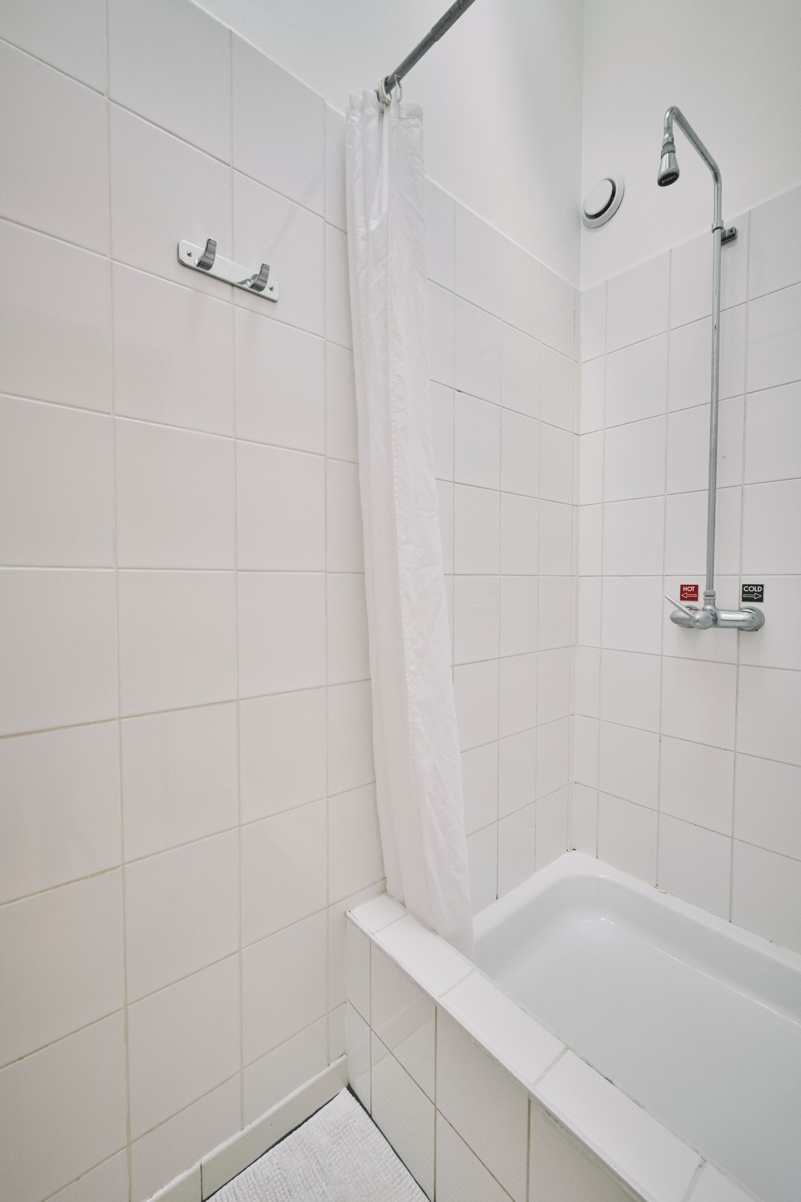 Une salle de bain avec des carreaux blancs, une douche avec un rideau et une baignoire avec un robinet.
