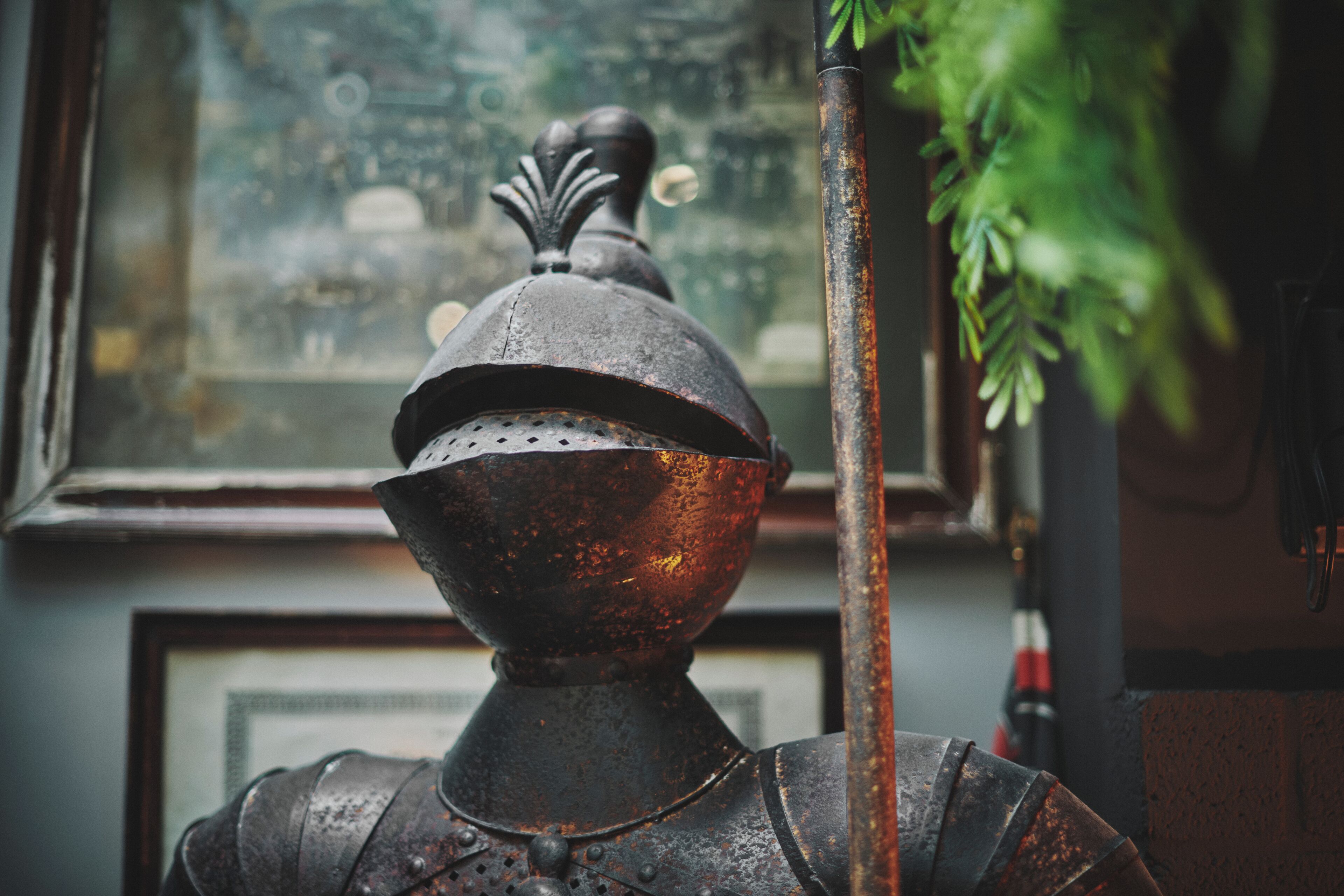 Un objet en métal ancien et rustique, orné d’un élément décoratif sur le dessus, qui pourrait faire partie d’une structure plus vaste, le tout mis en valeur sur un fond flou comprenant une fenêtre et de la verdure.