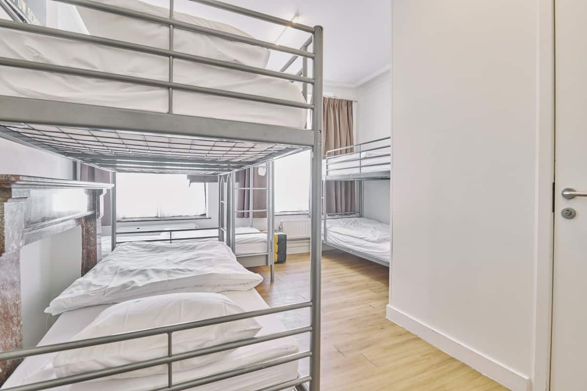 Een studentenkamer met stapelbedden, een raam met gordijnen en een deur.
