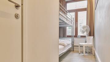Une chambre avec un lit superposé, une fenêtre, un radiateur, une chaise et une porte dotée d’une poignée et d’une serrure.