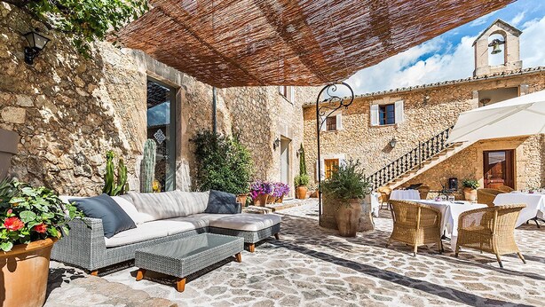 A stone courtyard with outdoor seating, a staircase, and a bell tower. - Reads Balance Hotel (Santa Maria del Camí)