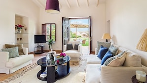 A spacious living room with a large window, a television, and a coffee table with decorative items. - Reads Balance Hotel (Santa Maria del Camí)