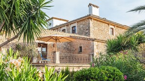 A stone building with a balcony, surrounded by lush greenery and flowering plants. - Reads Balance Hotel (Santa Maria del Camí)