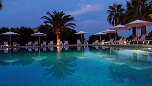 A swimming pool with lounge chairs and umbrellas, surrounded by palm trees. - Reads Balance Hotel (Santa Maria del Camí)