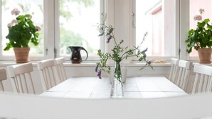 A white dining table with a clear glass vase containing purple flowers, surrounded by white chairs.