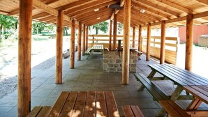 A covered picnic area with wooden benches and picnic tables, stone pillars, and a stone wall.