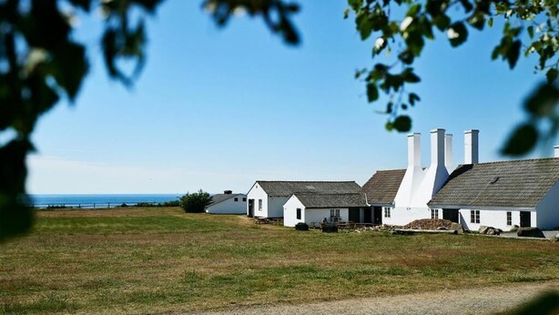 A row of white buildings with chimneys, a gravel path, and a view of the sea.