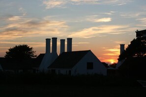 A silhouette of a building with multiple chimneys against a sunset sky.