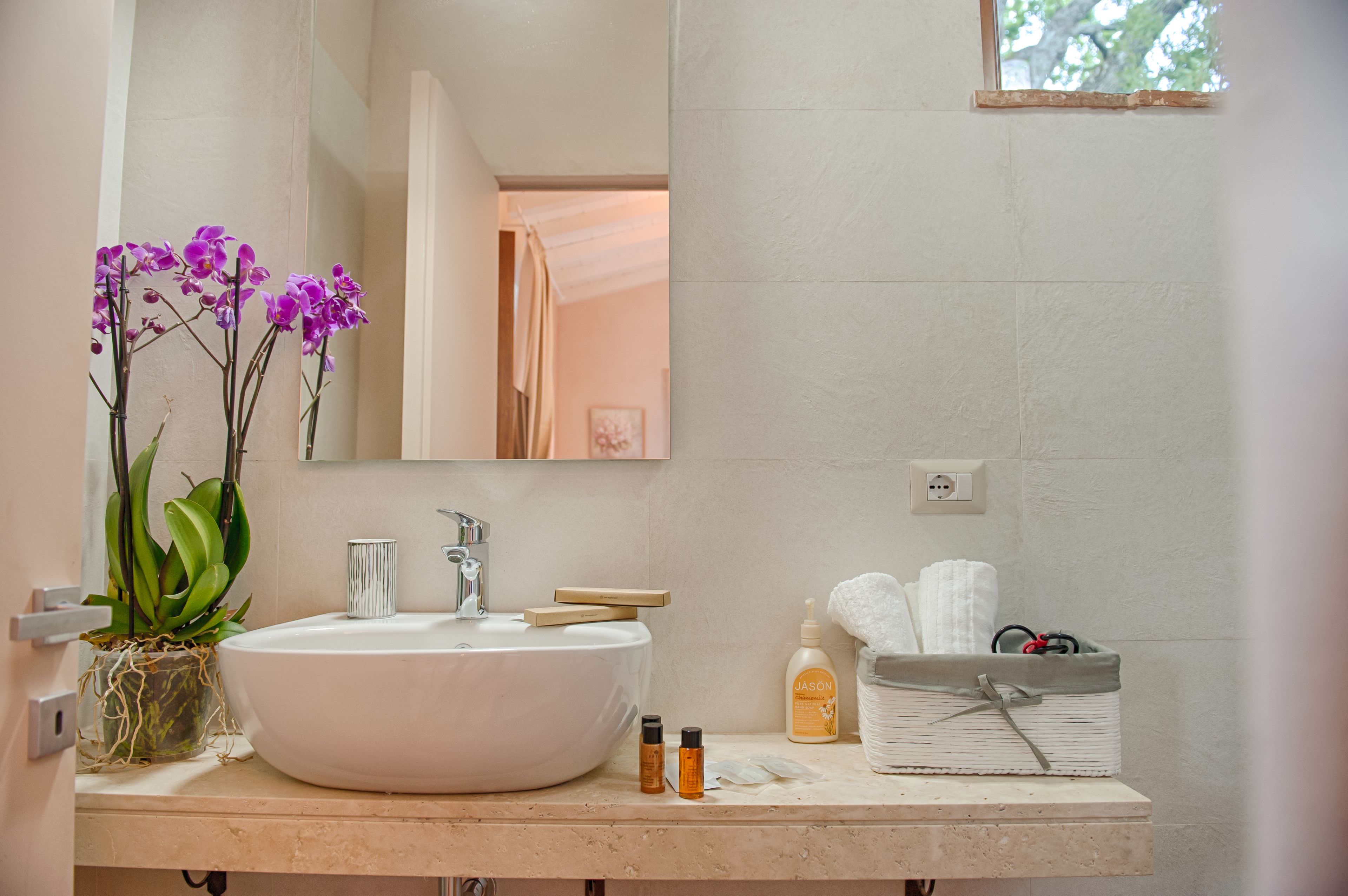 A bathroom with a white sink, mirror, and a potted orchid. There are toiletries and towels on the counter.