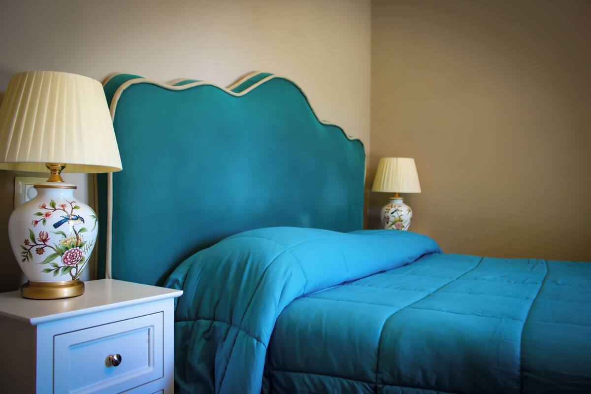 A bedroom with a teal headboard, a white nightstand with a lamp, and a matching bed.