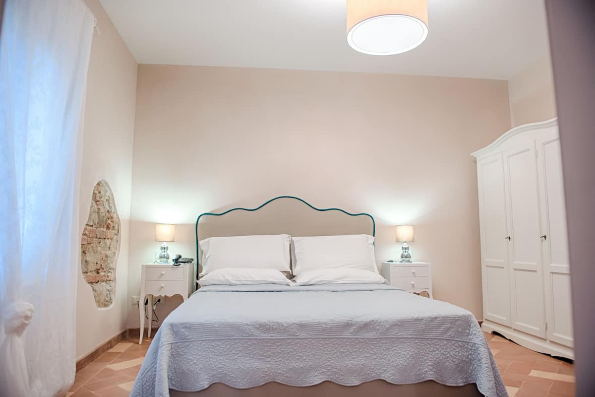 A bedroom with a bed, bedside lamps, a wardrobe, and a wall with a decorative element.