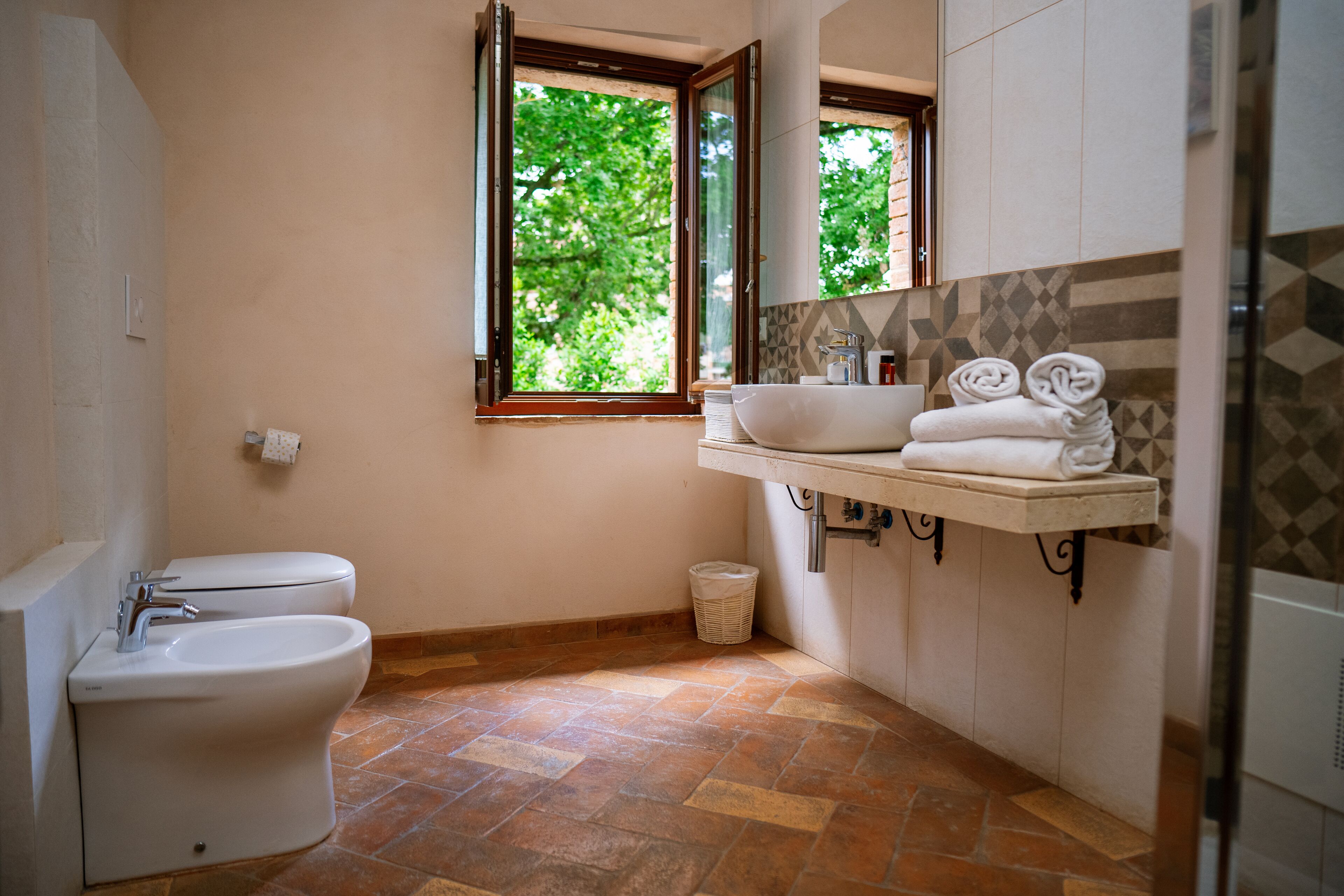 Un bagno con servizi igienici, bidet, lavandino e una finestra vista alberi.