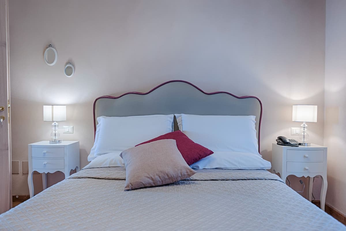 A neatly made bed with white and red pillows, two bedside tables with lamps, and a simple headboard.