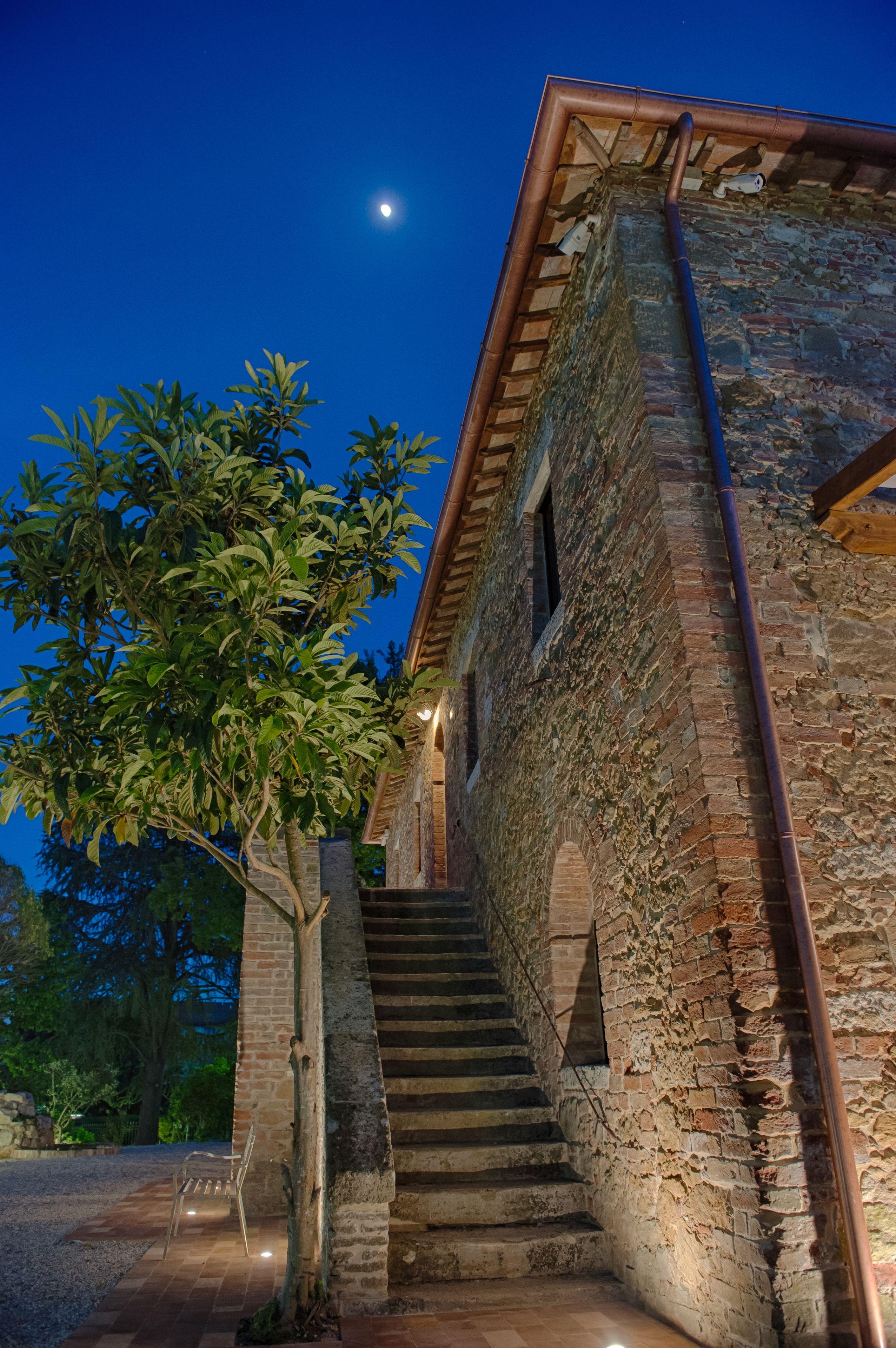 Un edificio in pietra con una scala che conduce a una porta, circondato da alberi e un cielo sereno.