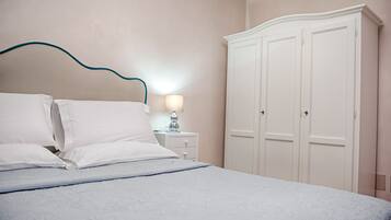 Un letto rifatto con lenzuola bianche, una lampada da comodino e un armadio bianco.