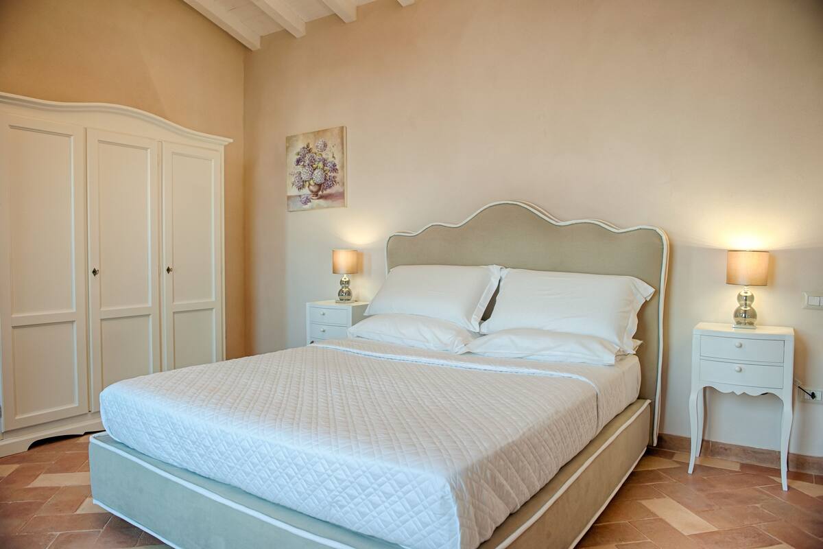 A neatly made bed with white bedding, two bedside tables with lamps, and a wardrobe.