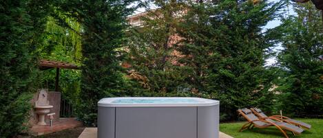 A hot tub in a garden with a brick wall and a statue.
