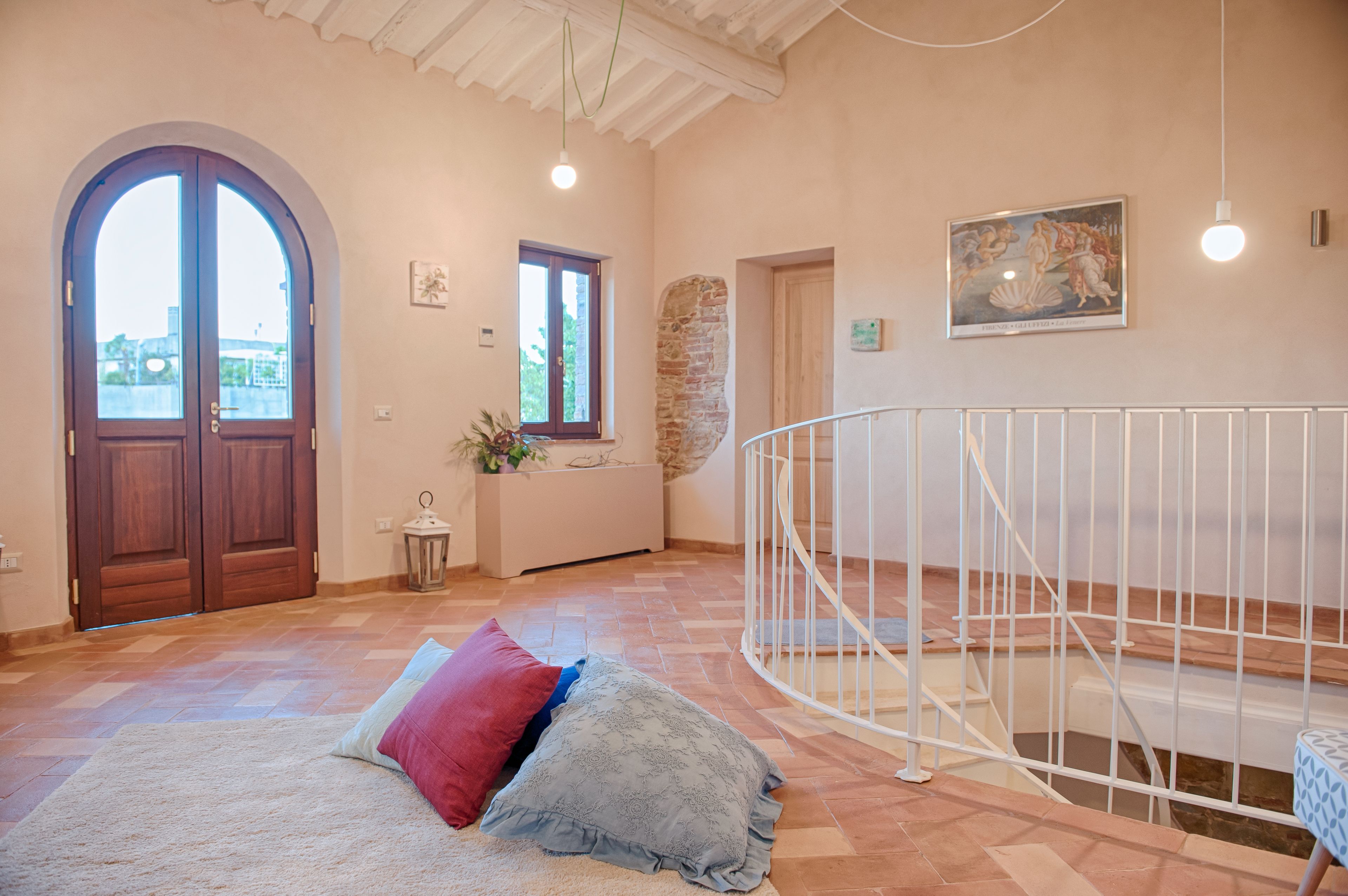 A spacious room with a wooden door, a stone wall, a white railing, and a view through a window.