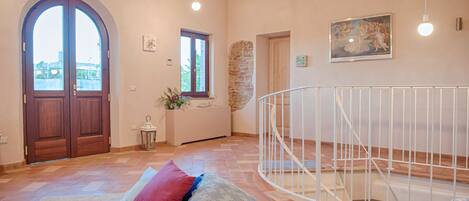 A spacious room with a wooden door, a stone wall, a white railing, and a view through a window.