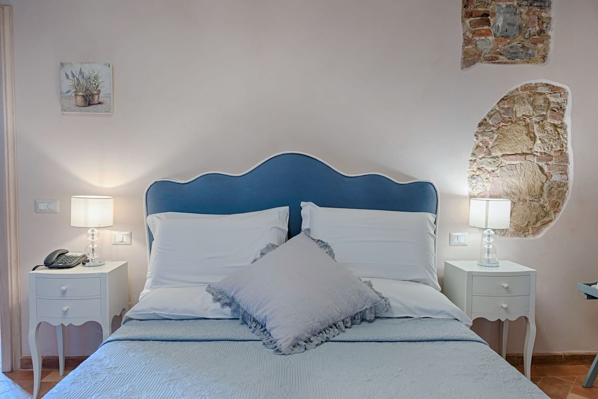 A neatly made bed with white linens and a blue headboard, flanked by two bedside tables with lamps and a phone.