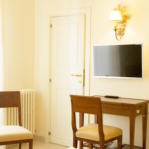 A room with a white door, a wooden desk with a chair, a flat-screen TV, and a wall-mounted lamp. - Hotel Lanzillotta (Alberobello)