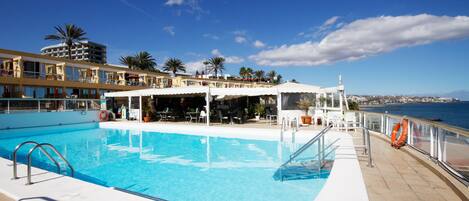 A swimming pool with a lifebuoy, a covered seating area, and a view of the sea.