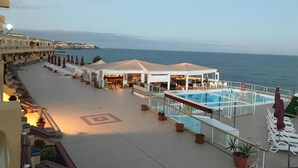 A rooftop terrace with a pool, lounge chairs, and a dining area overlooking the sea.