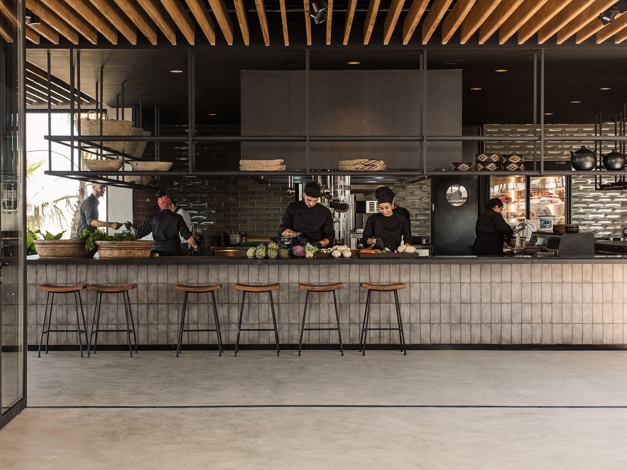 Una cocina moderna con chefs preparando comida, taburetes de bar de madera y un revoque de ladrillo.