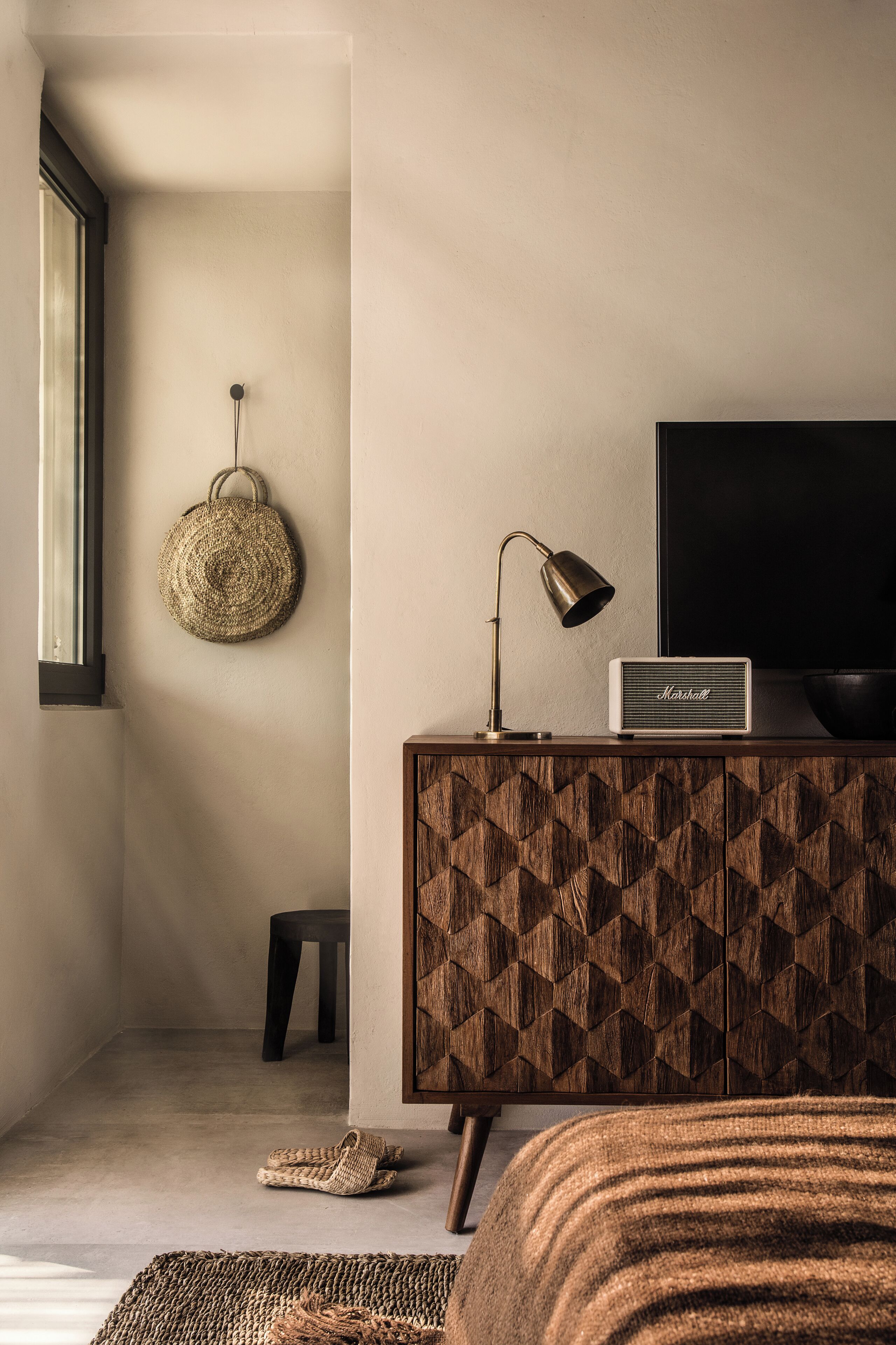 Een moderne slaapkamer met een houten kast, een televisie, een lamp en een geweven mand aan de muur.