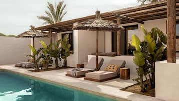 Un espace aménagé au bord de la piscine, avec des chaises longues, des parasols et des plantes tropicales.