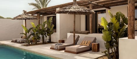 A poolside area with lounge chairs, umbrellas, and tropical plants.
