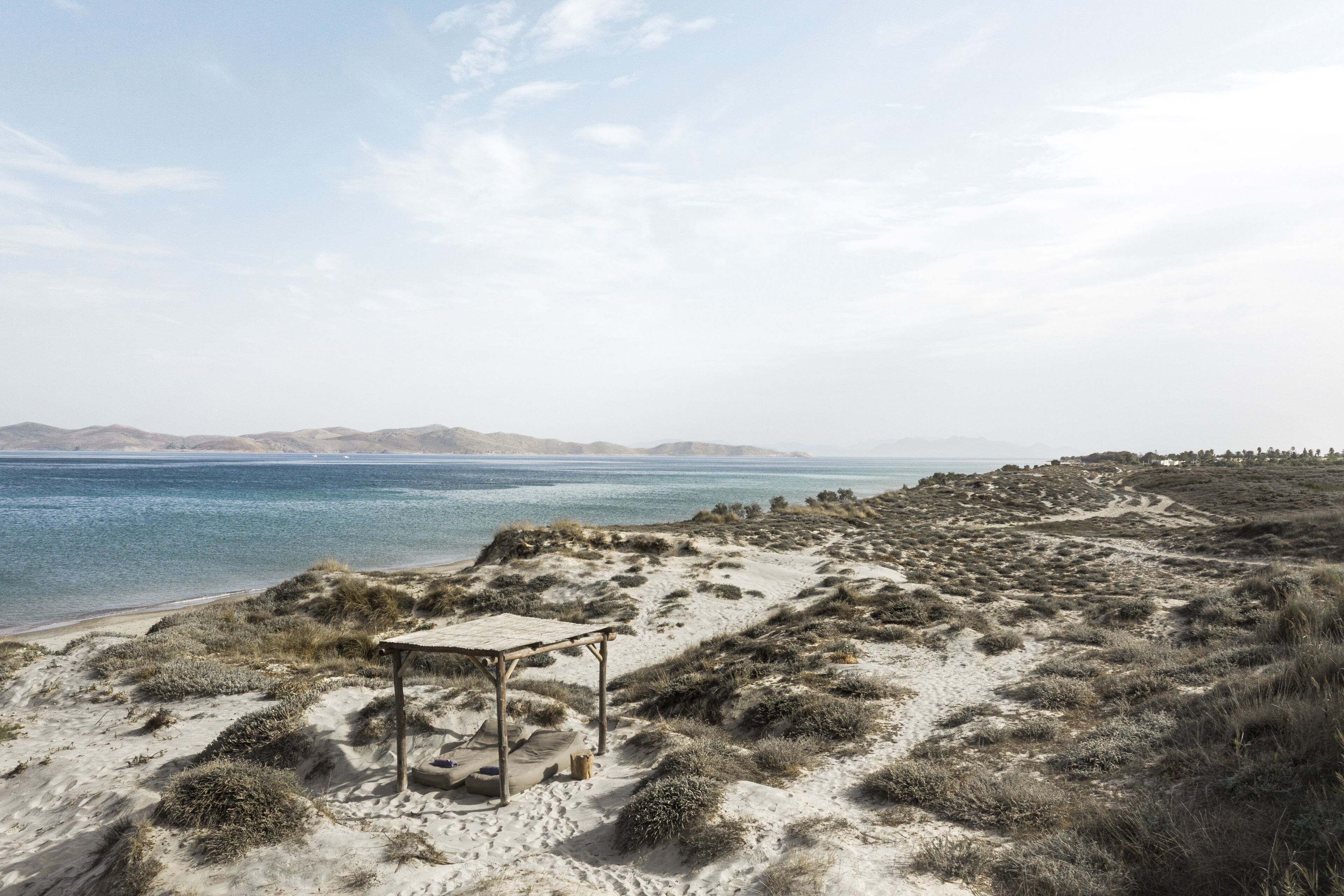 A beach with a wooden structure, sandy dunes, and a view of the sea and distant hills.