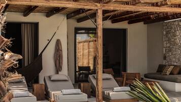 Un espace aménagé au bord de la piscine, avec des chaises longues, un hamac et un mur en pierre.