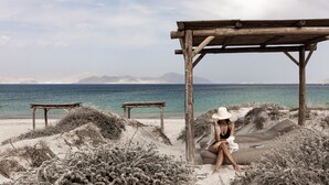 A beach scene with a wooden structure, a bench, and a person sitting on a sand dune.