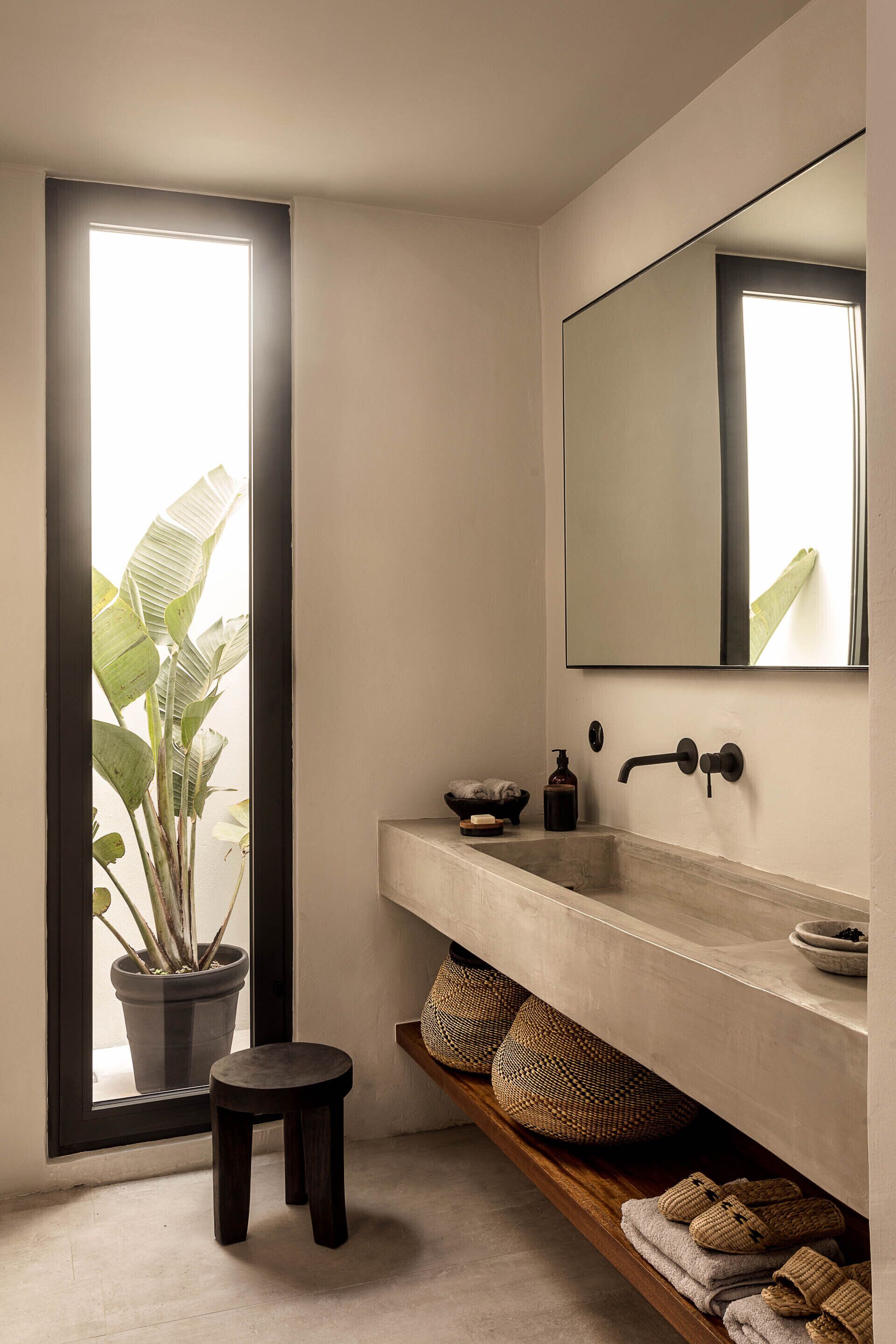 A bathroom with a large window, a potted plant, a sink, and a mirror.